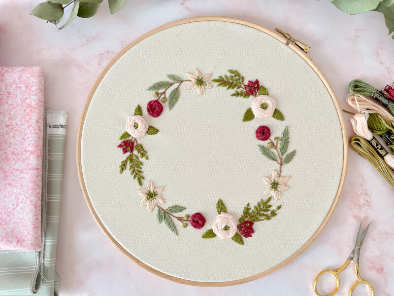 an embroidery hoop filled with fabric embroidered with flowers sits on a table with scissors next to it